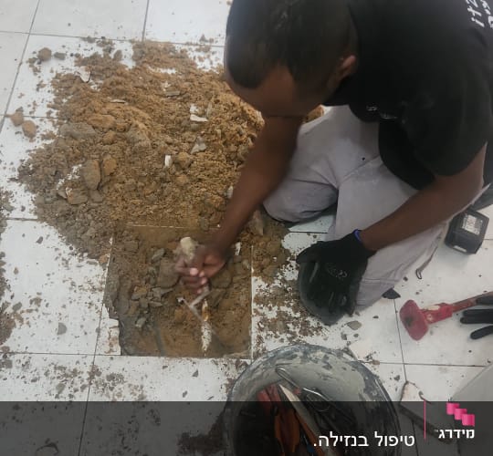 אדם חופר ברצפה עם כלים ודלי מלא כלי עבודה